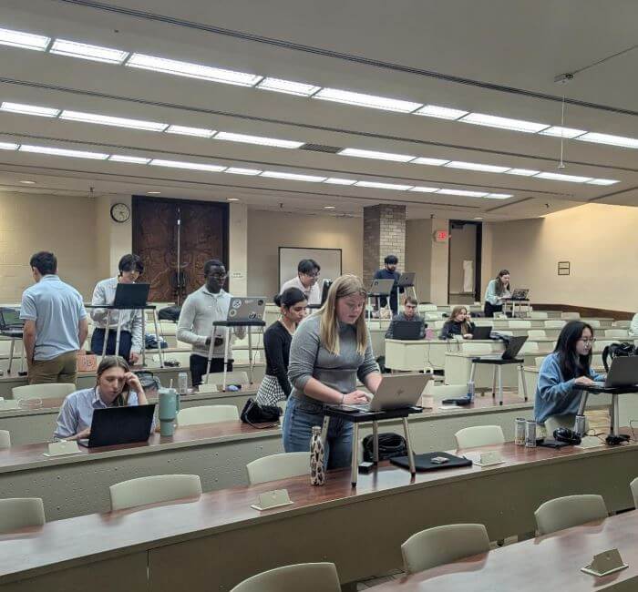 Diverse college debaters preparing for NFA competition, focused on laptops in a modern lecture hall.