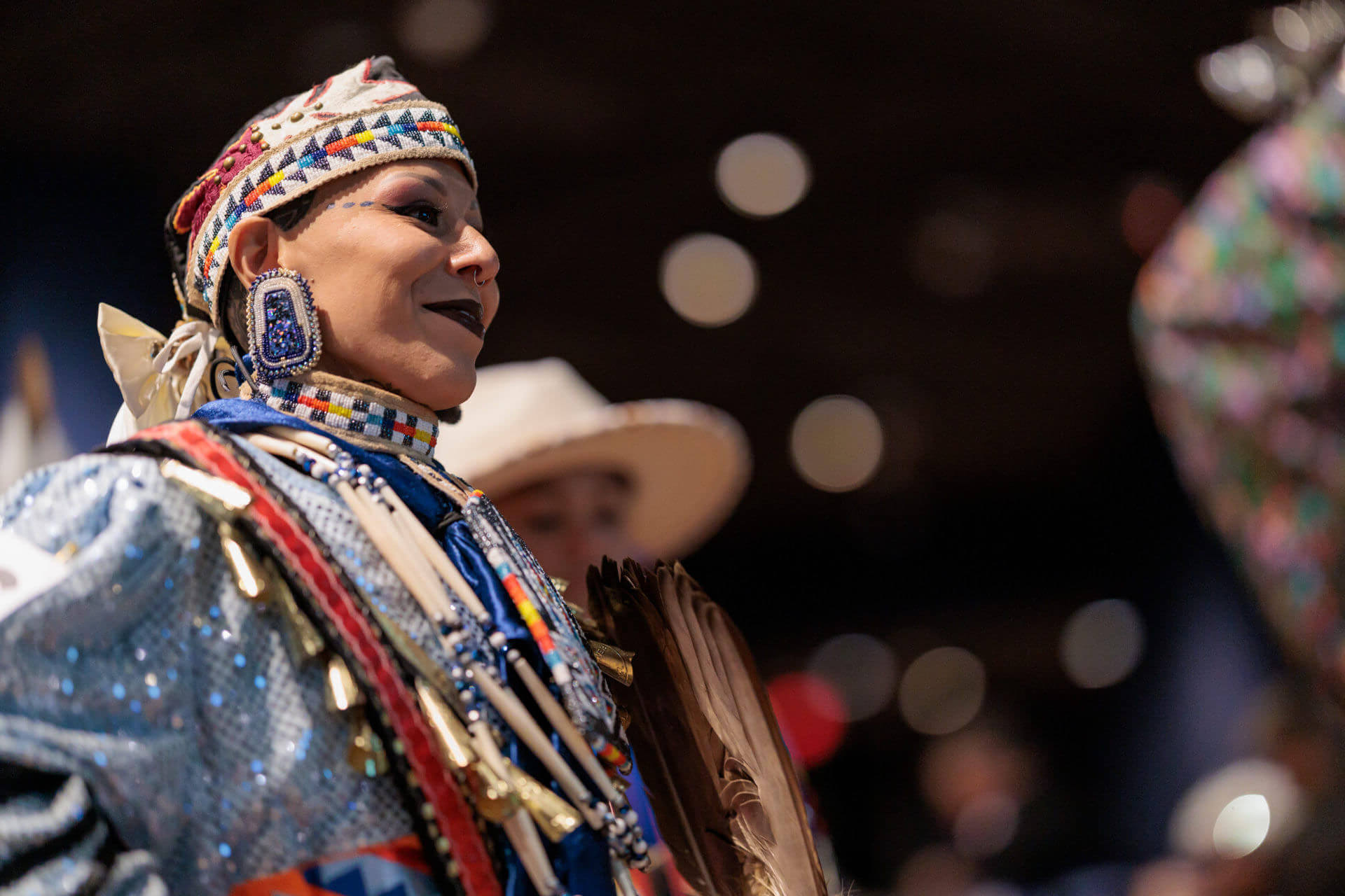 Native American woman in elaborate beaded powwow regalia, headdress, and ceremonial feather fan at Milwaukee Public Museum.