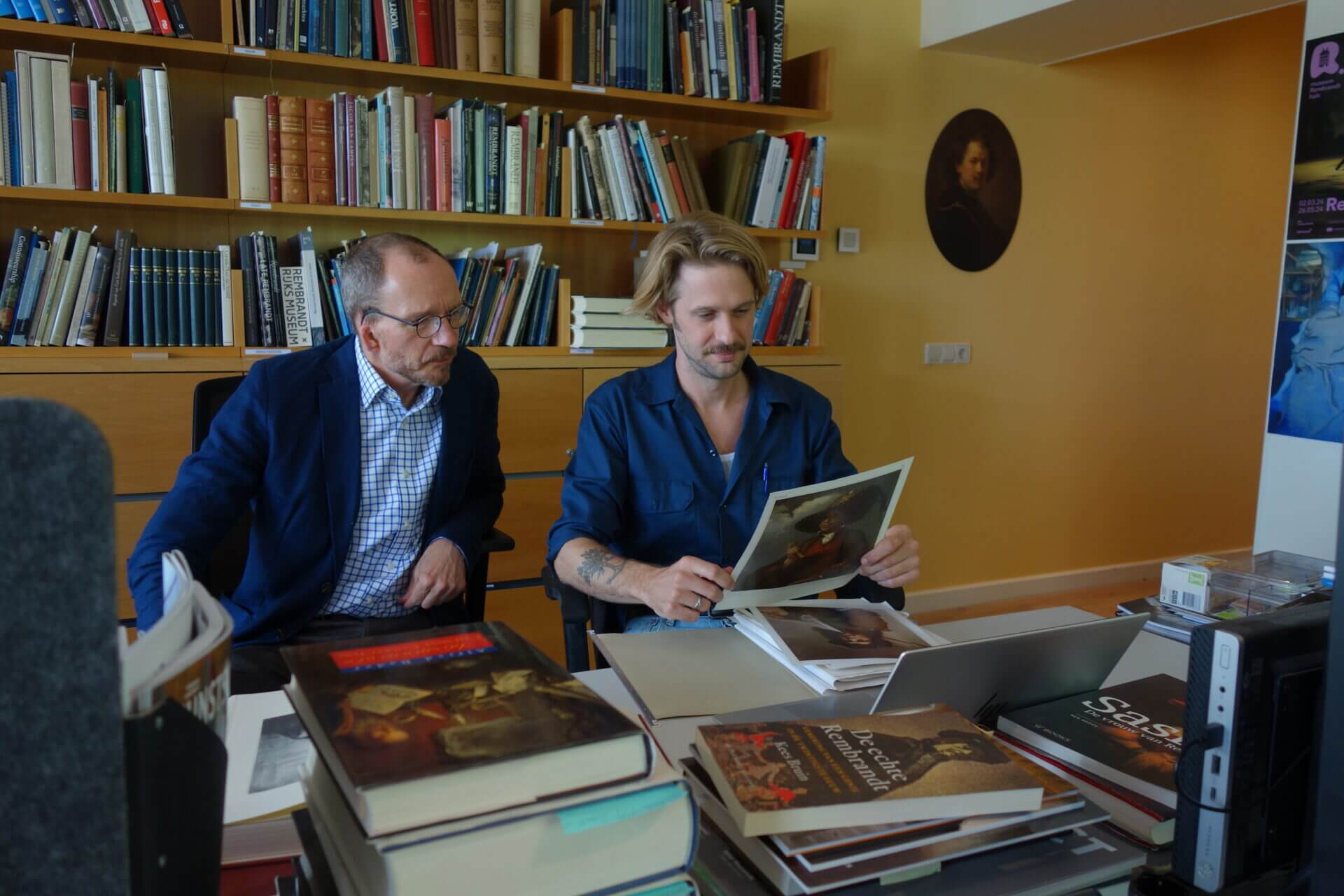 Art researchers at Rembrandt House examine a Rembrandt painting print, surrounded by art history books for the 2025 legacy.