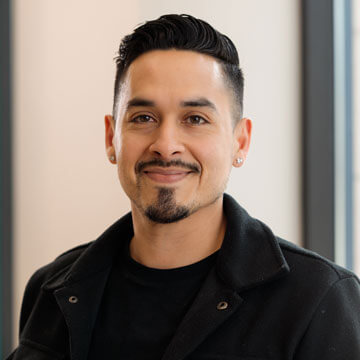 Adrian Hernandez, smiling professional in a grey blazer over a blue hoodie with dark hair and goatee.