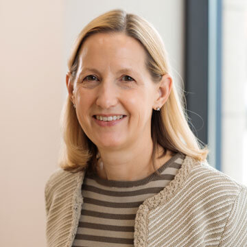Audra Brennan smiling professional blonde woman wearing a multi-strand pearl necklace.