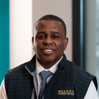 Adrian Hernandez, smiling professional in a grey blazer over a blue hoodie with dark hair and goatee.