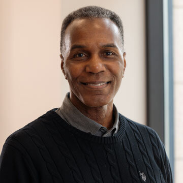 Clarence Johnson, smiling professional African American man in a grey suit and blue striped tie.