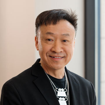 Yaa Engel smiling in glasses with long dark hair, blue shirt, and distinctive wooden and blue feathered earrings.