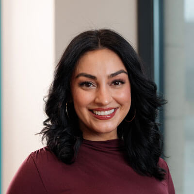 Smiling professional Latina businesswoman in black blazer. Confident corporate headshot, long dark hair, office setting.