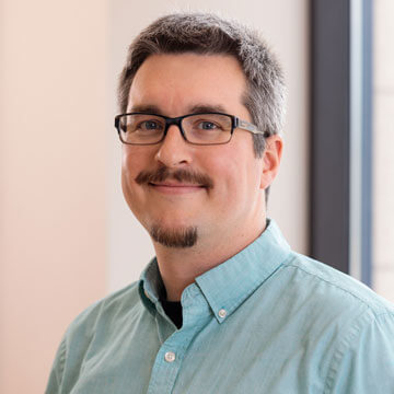 Nick Davis, smiling man in blue polo shirt, glasses, and goatee. Professional headshot.
