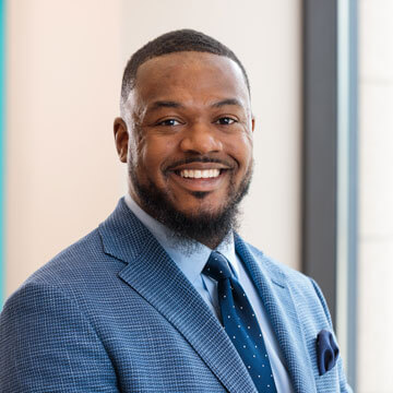 Vincent Mack, smiling Black man in a dark suit and tie, professional business headshot outdoors.