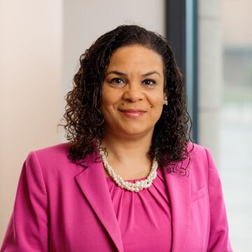 Jeannie Fenceroy, smiling business professional in a beige blazer, patterned blouse, and pearl necklace.